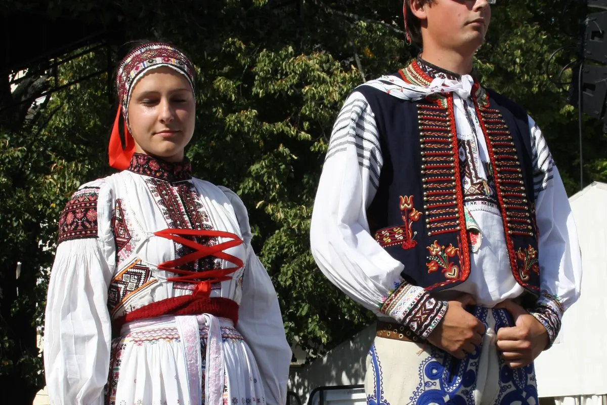 A young couple in festive Moravian Slovácko costume: embroidered white sleeves, a red and dark vest, a long embroidered apron and a dark waistcoat